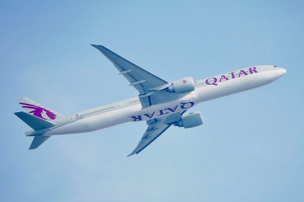 High-angle view of a Qatar Airways Boeing 777 airplane soaring in a clear blue sky, showcasing aviation elegance.
